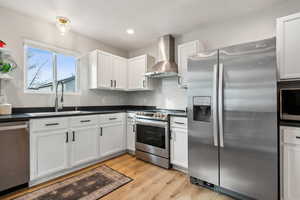 Kitchen with dark countertops, appliances with stainless steel finishes, wall chimney range hood, white cabinetry, and a sink