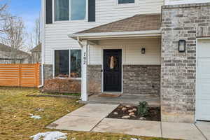 Doorway to property featuring a garage, a shingled roof, and fence