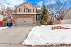 View of front facade featuring concrete driveway, brick siding, fence, and an attached garage