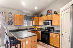 Kitchen with dark countertops, stainless steel microwave, electric range, a sink, and a kitchen bar