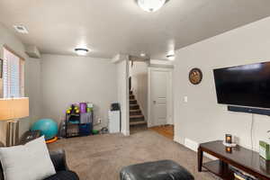 Living room featuring visible vents, light colored carpet, stairway, a textured ceiling, and baseboards