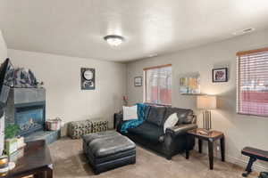 Carpeted living area featuring visible vents, a fireplace, a textured ceiling, and baseboards