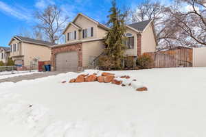 View of front of property featuring brick siding, an attached garage, and fence