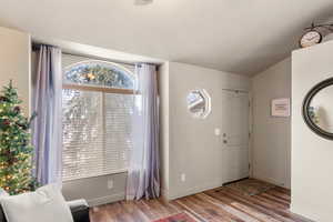 Entryway with lofted ceiling, wood finished floors, and baseboards