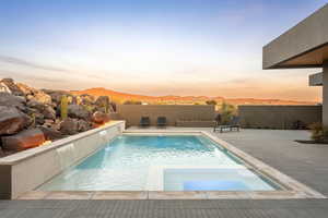 Pool at dusk featuring a pool with connected hot tub, fence, a mountain view, and a patio