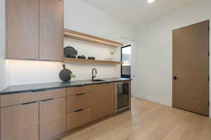 Bar with beverage cooler, baseboards, wet bar, light wood-style floors, and a sink