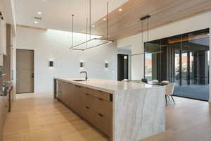 Kitchen featuring a sink, a large island, light wood finished floors, modern cabinets, and pendant lighting