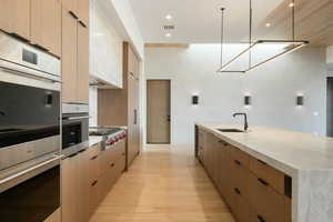 Kitchen with modern cabinets, hanging light fixtures, light brown cabinets, stainless steel gas cooktop, and a sink