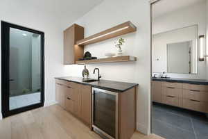 Bar featuring wine cooler, baseboards, a sink, and light wood finished floors