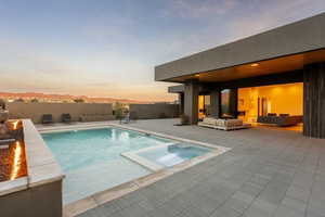 Pool at dusk featuring a mountain view, fence, a pool with connected hot tub, a patio area, and an outdoor living space with a fire pit