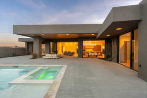 Back of house at dusk with a pool with connected hot tub, outdoor lounge area, and a patio