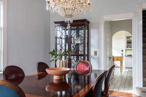 Dining area featuring light wood-style floors, arched walkways, and a notable chandelier