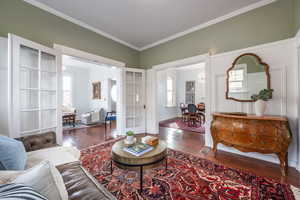 Living area featuring dark wood-style floors, crown molding, baseboards, and an inviting chandelier