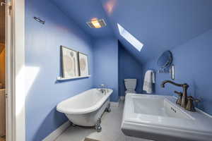 Bathroom featuring visible vents, toilet, a soaking tub, lofted ceiling with skylight, and a sink