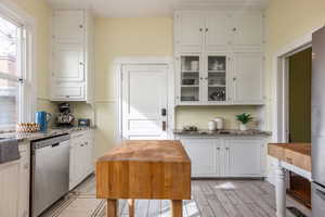 Kitchen featuring light stone counters, light wood finished floors, stainless steel dishwasher, glass insert cabinets, and white cabinets