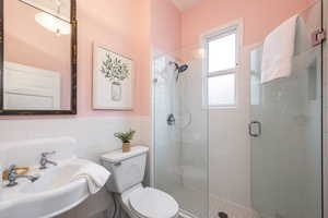 Full bathroom featuring tile walls, wainscoting, a shower stall, and toilet