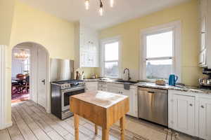 Kitchen with arched walkways, stainless steel appliances, white cabinetry, a sink, and light stone countertops