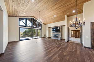 Unfurnished living room featuring a chandelier, wooden ceiling, dark wood-style flooring, a fireplace, and high vaulted ceiling