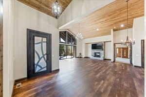 Entryway with wooden ceiling, dark wood-style floors, high vaulted ceiling, a stone fireplace, and a chandelier