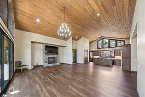 Unfurnished living room featuring high vaulted ceiling, a stone fireplace, wood ceiling, and an inviting chandelier