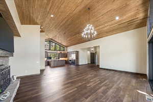 Unfurnished living room featuring wooden ceiling, dark wood-style floors, a fireplace, high vaulted ceiling, and a notable chandelier