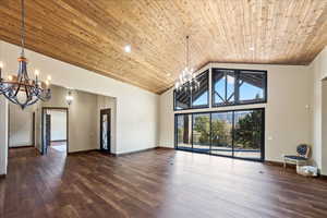 Empty room featuring high vaulted ceiling, wooden ceiling, a notable chandelier, baseboards, and dark wood finished floors