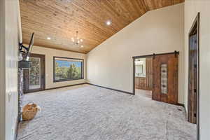 Empty room with high vaulted ceiling, wood ceiling, light carpet, and a barn door