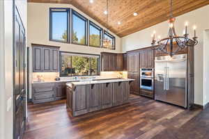 Kitchen featuring stainless steel appliances, decorative light fixtures, a kitchen island, and light stone countertops