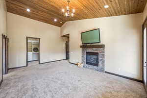 Unfurnished living room with light colored carpet, wood ceiling, a stone fireplace, high vaulted ceiling, and baseboards