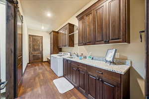 Laundry area featuring a barn door, dark wood-style flooring, a sink, baseboards, and cabinet space