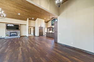 Unfurnished living room with high vaulted ceiling, a notable chandelier, dark wood-type flooring, a fireplace, and wood ceiling