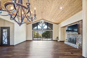 Unfurnished living room featuring dark wood finished floors, lofted ceiling, wood ceiling, a stone fireplace, and a chandelier