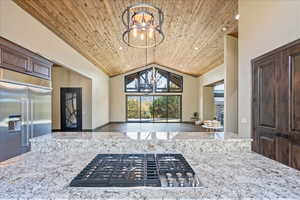 Kitchen featuring dark brown cabinetry, a notable chandelier, stainless steel appliances, wood ceiling, and light stone countertops