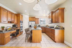 Kitchen with appliances with stainless steel finishes, brown cabinetry, built in study area, a kitchen island, and a kitchen breakfast bar