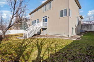 Rear view of house with stairs, fence, a lawn, and stucco siding