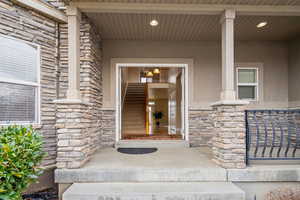 Entrance to property with stone siding, a porch, and stucco siding