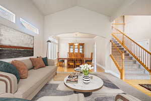 Living area featuring arched walkways, high vaulted ceiling, stairway, and light wood-style floors