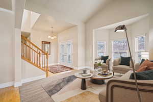 Living room featuring an inviting chandelier, stairs, baseboards, and wood finished floors