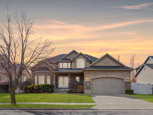 View of front facade featuring an attached garage, driveway, stone siding, a lawn, and stucco siding