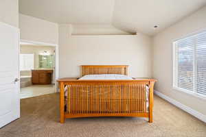 Bedroom with lofted ceiling, visible vents, ensuite bathroom, light carpet, and baseboards