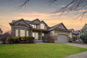 View of front of house featuring an attached garage, stone siding, a front lawn, and stucco siding