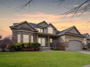 View of front of house featuring an attached garage, stone siding, a front lawn, and stucco siding