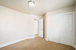 Unfurnished bedroom featuring light carpet, a closet, and baseboards