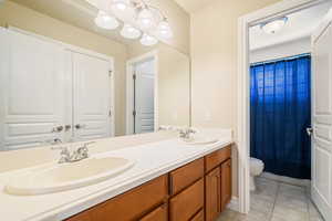 Full bath featuring double vanity, a sink, toilet, and tile patterned floors