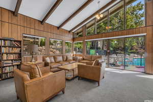 Living area featuring high vaulted ceiling, wood walls, carpet flooring, and beam ceiling