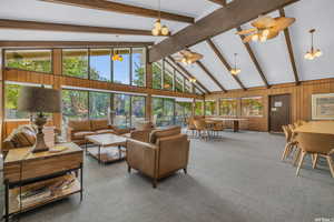 Living area with a ceiling fan, beamed ceiling, carpet, wood walls, and high vaulted ceiling