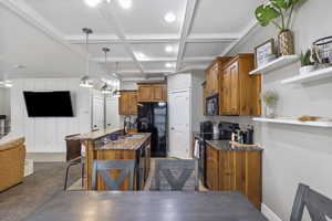 Kitchen featuring a breakfast bar, coffered ceiling, open floor plan, black appliances, and a center island with sink