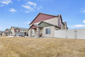 Exterior space featuring stone siding, a residential view, a gate, fence, and a yard