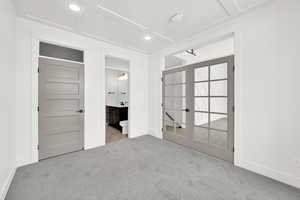 Unfurnished bedroom featuring baseboards, french doors, ensuite bathroom, and light colored carpet