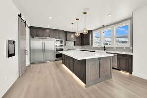 Kitchen with built in appliances, a barn door, dark brown cabinetry, a kitchen island, and hanging light fixtures